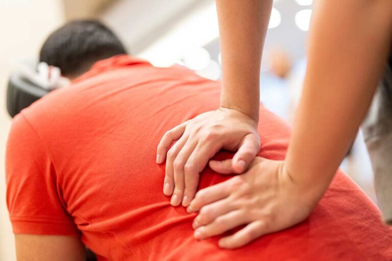 Person in comfortable clothing discussing health notes with a chiropractor in an exam room.