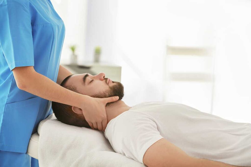 A chiropractor using a metal tool to treat a patient's forearm in a calm clinical setting.